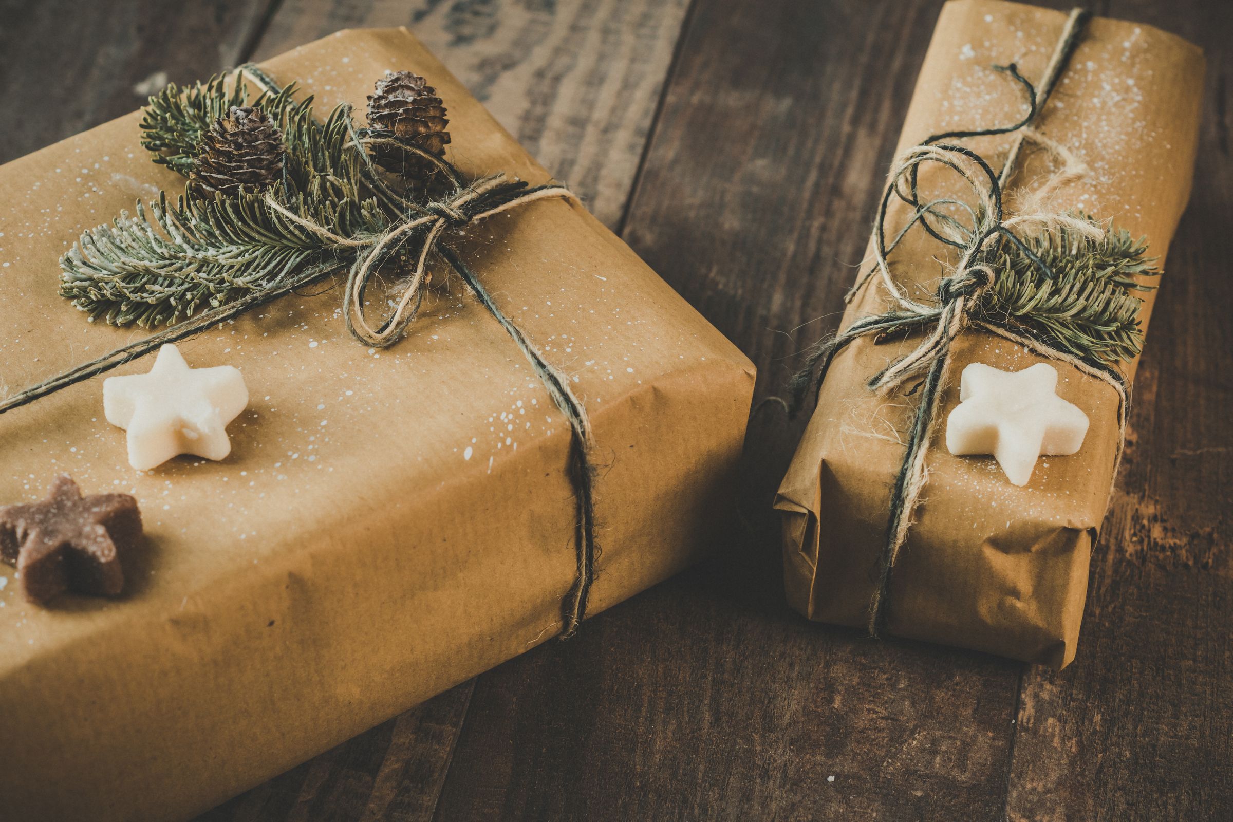 Two gifts wrapped in brown kraft paper and tied with string, with sprigs of fir, on a wooden table